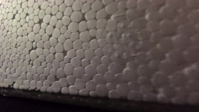 Close-up panning footage showcasing the detailed cellular pattern of expanded polystyrene (EPS) styrofoam. Features smooth white beads with subtle light gradients and shadows. Excellent for background