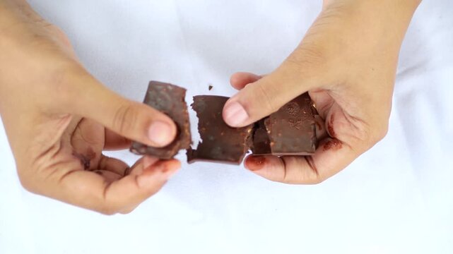 Hands breaking apart chocolate bar with nuts into two pieces