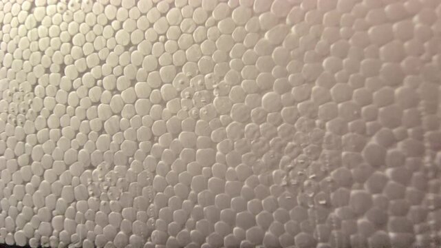 Close-up panning footage showcasing the detailed cellular pattern of expanded polystyrene (EPS) styrofoam. Features smooth white beads with subtle light gradients and shadows. Excellent for background