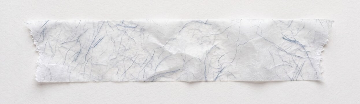 A piece of crumpled white tissue paper lies on a smooth, light grey surface, showcasing subtle textures and delicate folds in a minimalist composition.