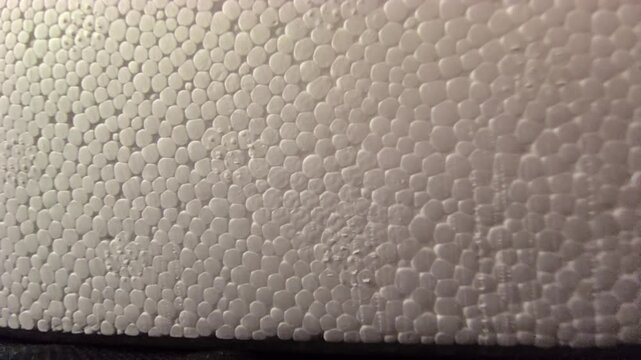 Close-up panning footage showcasing the detailed cellular pattern of expanded polystyrene (EPS) styrofoam. Features smooth white beads with subtle light gradients and shadows. Excellent for background