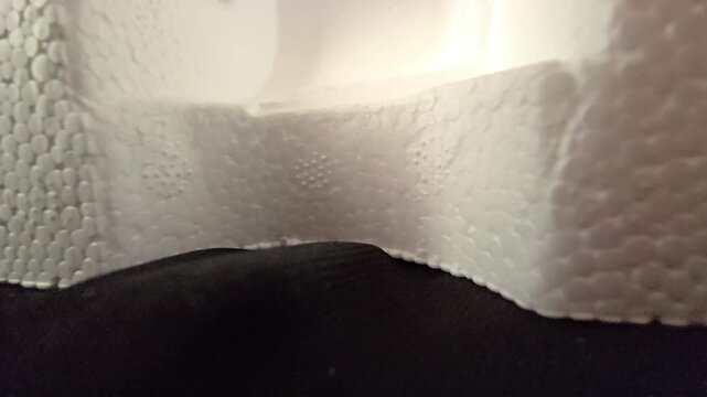 Close-up footage of a molded white styrofoam packaging container showing smooth curved edges and detailed cellular texture uder warm ambient light. Great for product packaging themes,