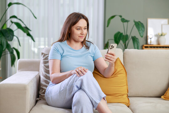 Woman browsing smartphone while relaxing at home