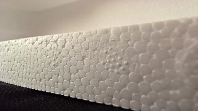 Side-angle macro video of a white polystyrene styrofoam block edge, showcasing its linear cellular structure and soft bright lighting. Ideal for material backgrounds, packaging designs, and industrial