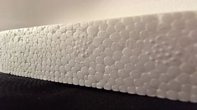 Side-angle macro video of a white polystyrene styrofoam block edge, showcasing its linear cellular structure and soft bright lighting. Ideal for material backgrounds, packaging designs, and industrial