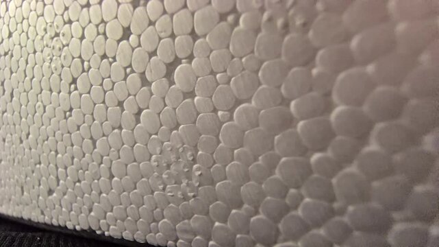 A close-up macro tracking shot over the bumpy, porous surface of white expanded polystyrene foam, highlighting its intricate cellular bead texture under warm studio side lighting.