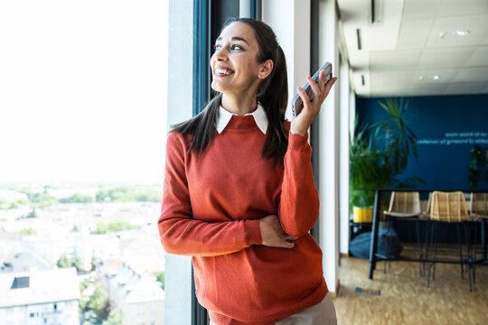 Smiling businesswoman holding mobile by office window