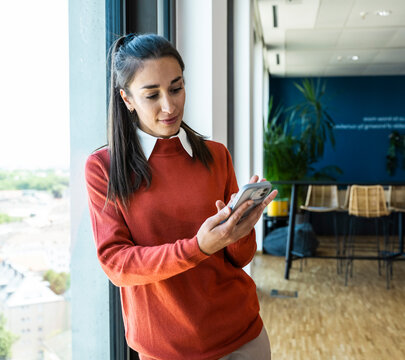 Businesswoman reads a message on her smartphone by the office window