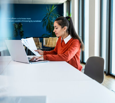 Businesswoman reads document and types on laptop at the office