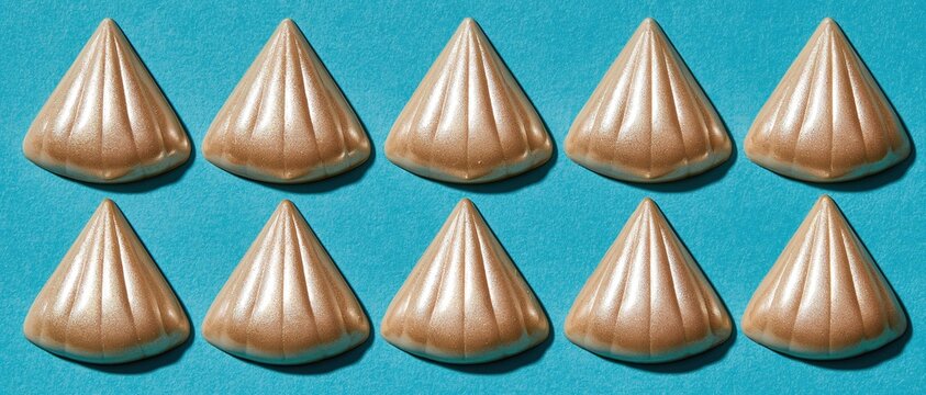 Symmetric repeating geometric pattern of ten golden glittery shell shaped textured pieces arranged in two even rows on plain solid bright blue background