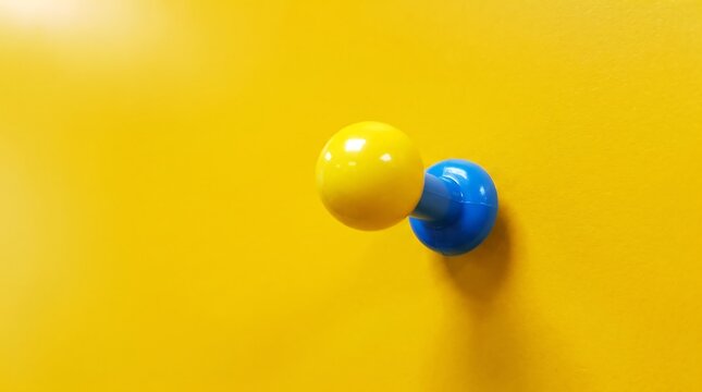 Vibrant yellow push pin on matching background, blue plastic thumbtack detail, minimalist office stationery concept for reminders