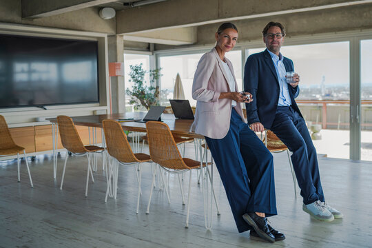 Businessman and businesswoman lean against a table in the office