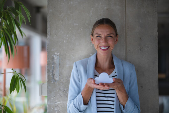 Smiling businesswoman holds a cloud symbol indoors
