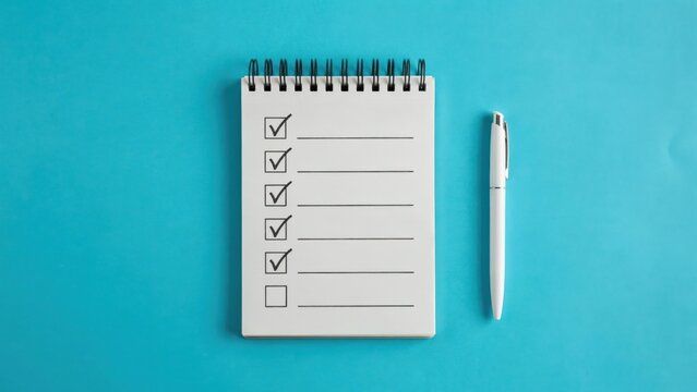 A white spiral notebook with completed checkmarks on lined paper beside a pen on a vibrant blue background. Great for productivity and to-do list concepts.