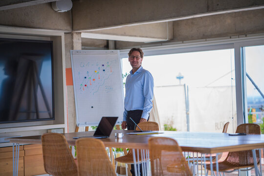 Smiling businessman standing at flipchart in modern startup office