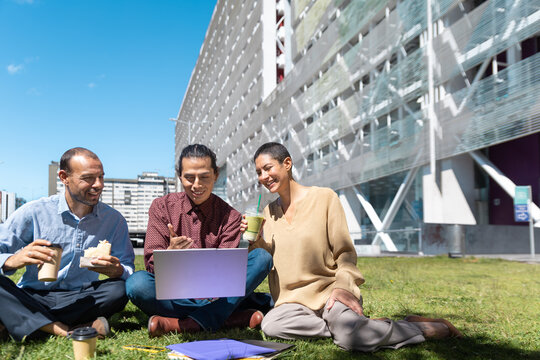 Colleagues share a lunch break on the grass with a laptop