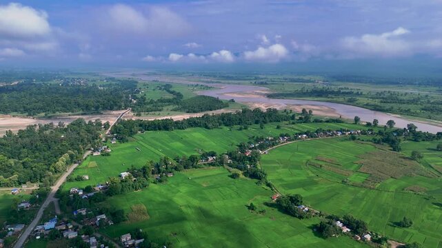 Expansive aerial view of a rural village and green farmland situated dangerously close to a massive flooded river basin in Nepal
