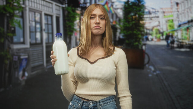 Young woman holds milk bottle with hand and visible cleavage on street; disapproval sustainability urban.