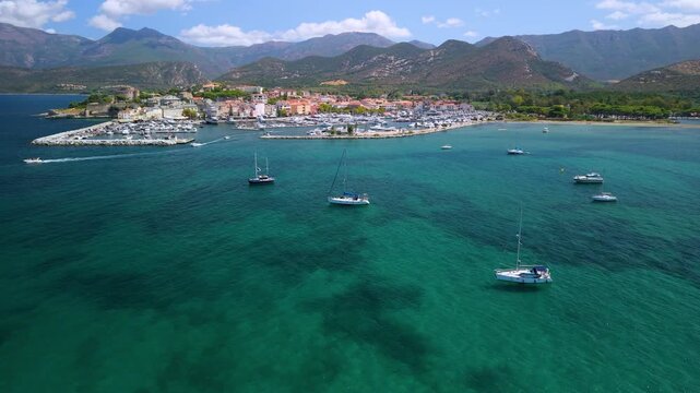 Saint-Florent Corsica drone flyover turquoise sea yachts motorboats pastel town, dynamic flight over harbor marina, white water wakes, colorful seaside houses bright daytime in Cap Corse France 4k 