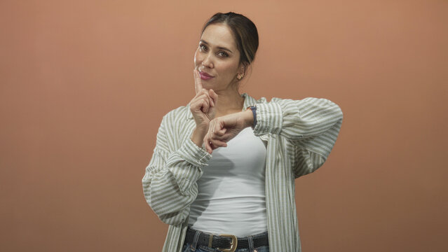 Woman points finger to wristwatch while checking time, casual striped shirt and white tank top visible in studio; impatience punctuality waiting.