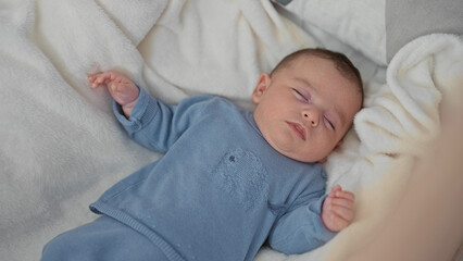 Boy sleeping with hands slightly raised on soft bed in building wearing blue onesie and cream blanket  serenity comfort. © Krakenimages.com