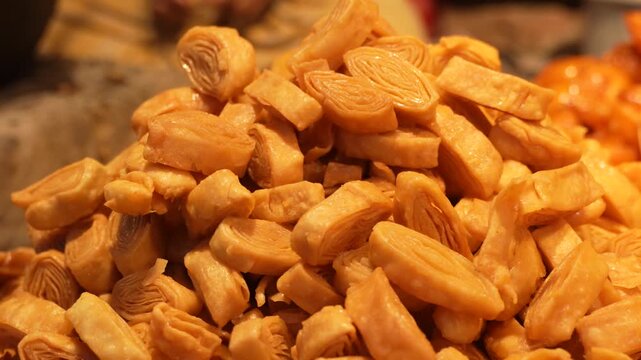 A close up view of a pile of golden crispy indian sweet called balushahi in a street food market.