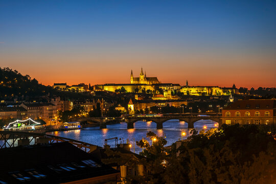The illuminated Prague castle overlooks the river at dusk