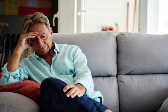 A stressed senior man sits on the living room sofa at home