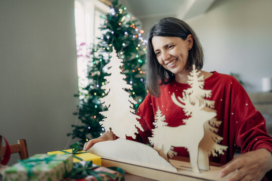 Smiling woman holds wooden reindeer decor at home during Christmas
