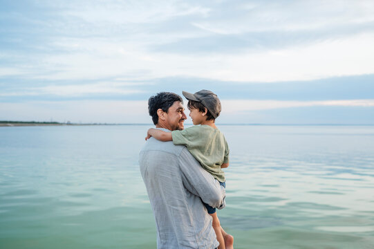 A father holds his son by the sea during a summer vacation