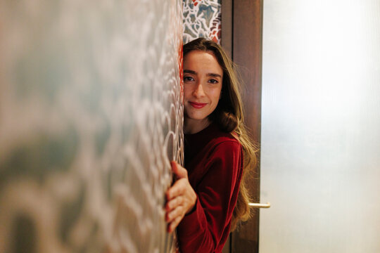 A happy young woman peeks around a hotel wall