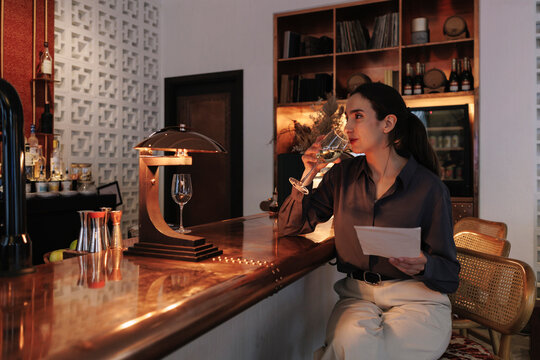 Woman drinks wine and reads menu at hotel bar
