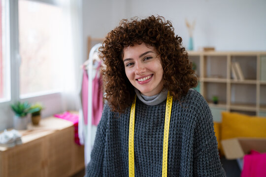 Smiling tailor with curly hair and measuring tape in home studio