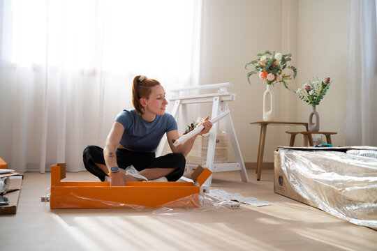 Woman sits on the floor assembling new furniture at home