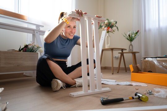 A woman assembles white wooden furniture on the floor at home