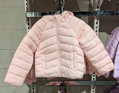Tiempo de oto&ntilde;o. Vista de frente de una chaqueta acolchada infantil con cremallera y capucha de color rosa colgada en una tienda de ropa