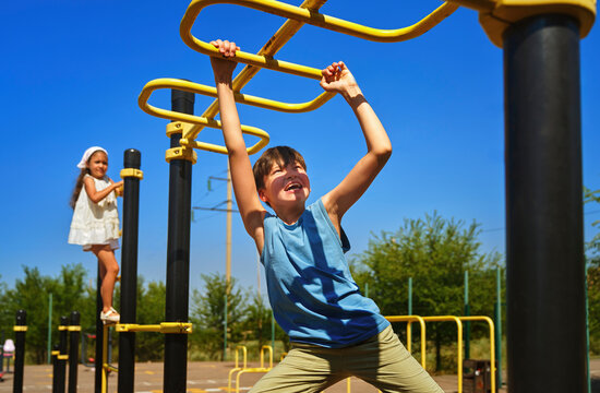 A boy and a girl play on a monkey bar at the outdoor playground