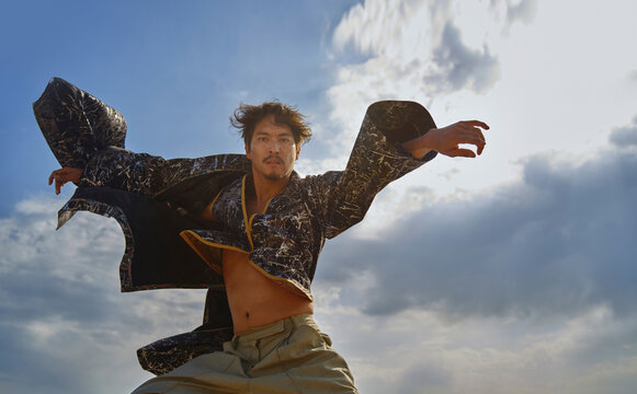 A man dances under the sky in a traditional patchwork robe
