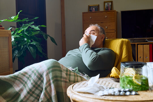Sick man blowing his nose while resting indoors at home