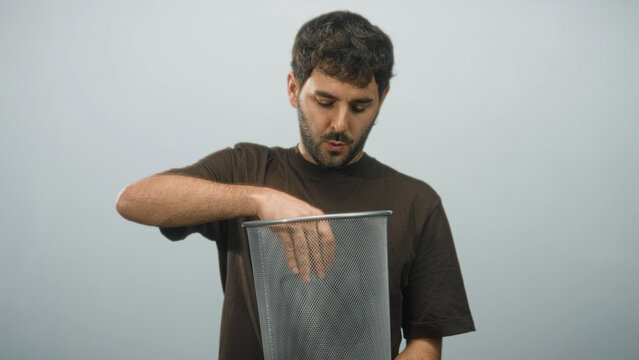 Hispanic man removes eyeglasses and drops them into a metal mesh bin with hand while peering inside in studio; satisfaction confidence success.