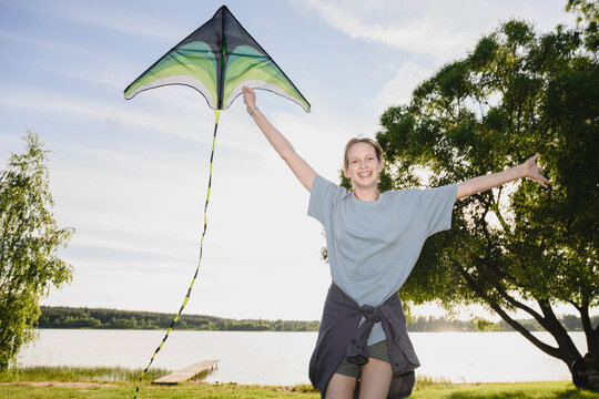 A smiling girl holds a kite by the lake during summer