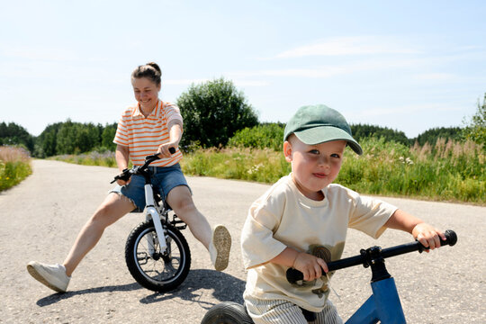 Mother and son ride balance bikes outdoors on a sunny summer day