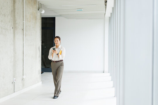 Businesswoman walks in a modern office hallway texting on mobile phone