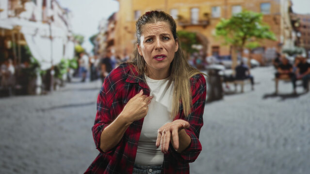 Woman pinching fingertips and holding palm up with pleading gesture, expressive face in a cobblestone street plaza; frustration.