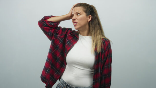 Woman touching forehead with hand, wearing red plaid shirt and white t shirt, looking perplexed in studio; frustration doubt.