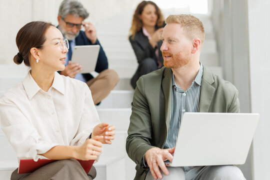 Business colleagues discuss work on office stairs with a laptop