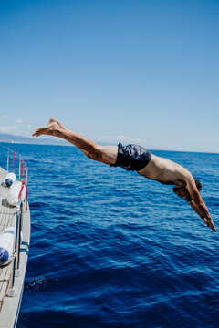 Man dives from a yacht into the blue sea during summer vacation