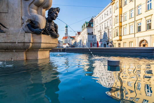The Hercules fountain reflects historic buildings in sunny Augsburg