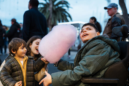 Happy boy in wheelchair holding cotton candy with family at the fair