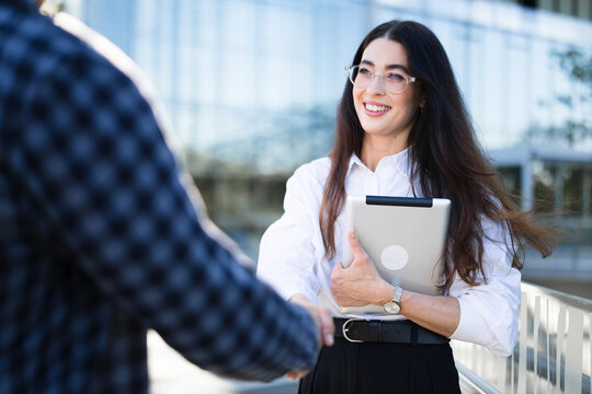 A smiling businesswoman shakes hands with a male colleague outdoors
